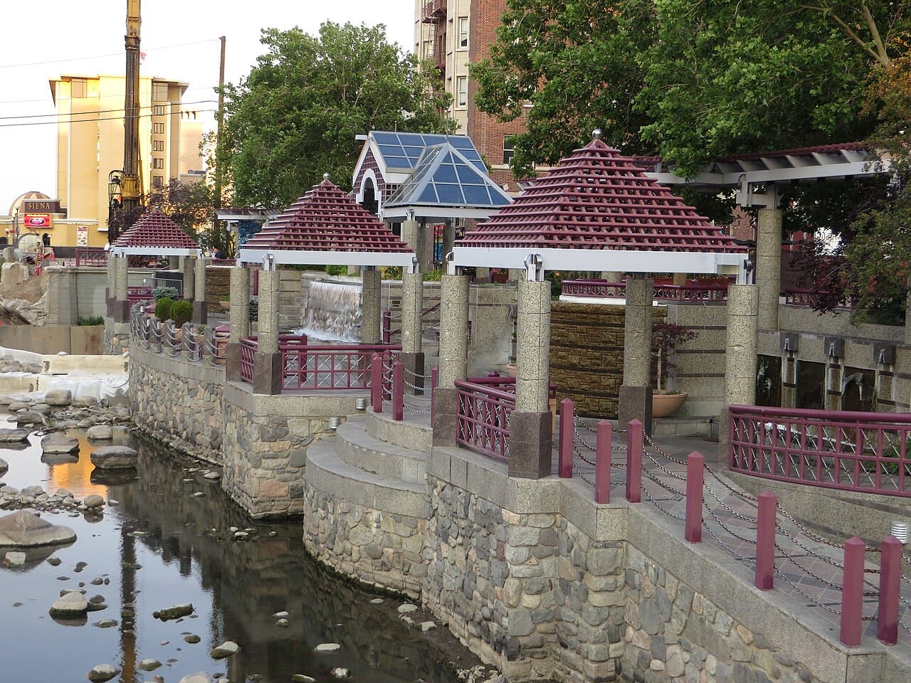 Stone-walled Truckee Riverwalk plaza in downtown Reno, with covered pergolas, a small waterfall, and the river running alongside.