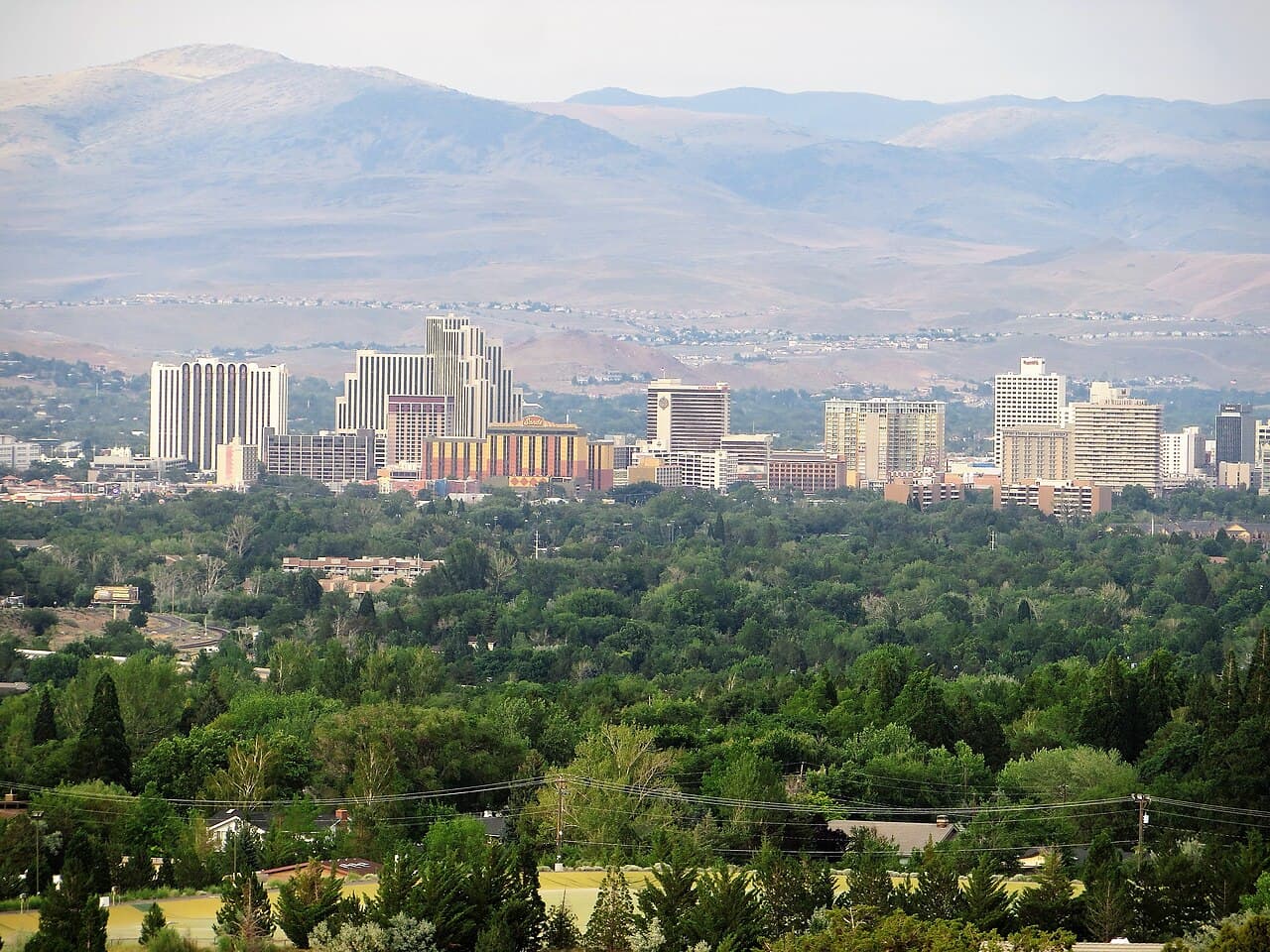 Downtown Reno's casino towers seen from Juniper Ridge, with the Sierra Nevada foothills rising behind the city and the Truckee Meadows in the foreground.